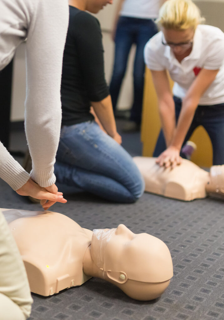 A group of adult education students practitcing CPR chest compressioon on a dummy.
