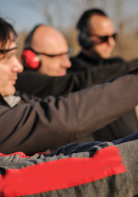 Group of people practice gun shoot on target on outdoor shooting range. Civilian team weapons training